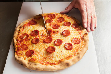 Wall Mural - A chef cuts freshly baked pizza just out of the hot oven,