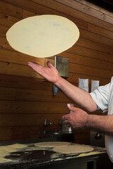 Wall Mural - A skillful chef is preparing pizza, twirling the dough, making thin crust for delicious Italian pizza in an upscale restaurant