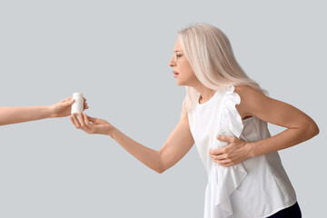 Sticker - Mature woman with heart attack taking pill bottle on grey background