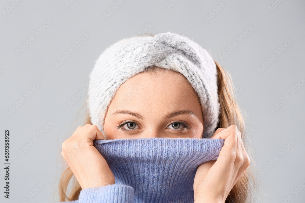 Frozen beautiful young woman in warm clothes on grey background