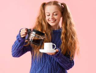 Poster - Beautiful young woman in warm sweater pouring coffee into cup on pink background