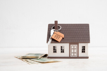 Poster - House figure with money, key and trinket on grunge white table near wall. Concept of buying real estate