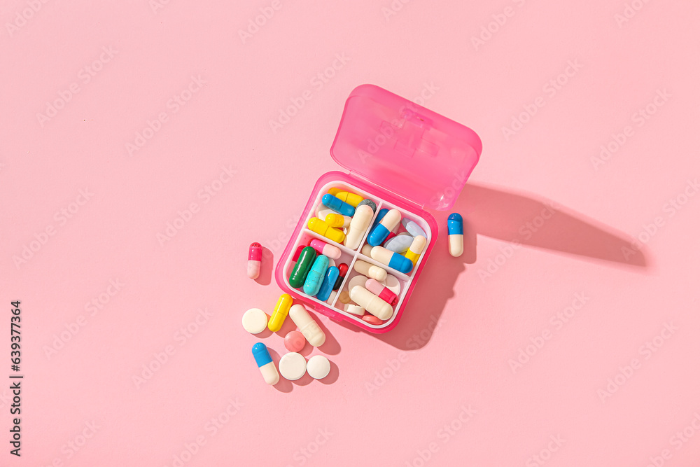 Container with different pills on pink background