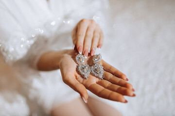 Wedding earrings on a woman's hand, she takes earrings, elegant bride's earrings, morning bride, white dress, wearing earrings