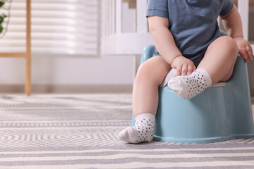 Little child sitting on plastic baby potty indoors, closeup. Space for text