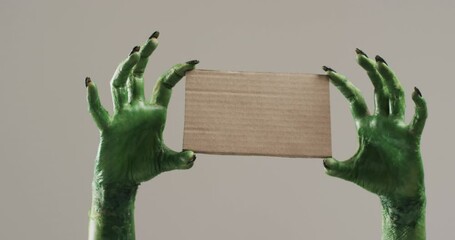 Poster - Video of halloween green monster hands holding card with copy space on grey background