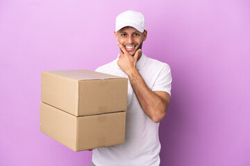 Wall Mural - Delivery caucasian man isolated on purple background happy and smiling