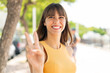 © luismolinero - Young woman at outdoors smiling and showing victory sign