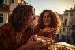 Young female friends eating pizza and smiling, sitting outside. Happy women enjoying street food in the city - Italian food culture Concept
