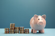 © vefimov - Piggy bank placed in front of neat stack of coins on blue background, illustrating idea of savings, financial planning, and wealth accumulation.