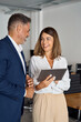 © Stock 4 You - Vertical portrait of mature Latin businessman and European businesswoman discussing project on tablet in office. Two diverse partners colleagues of confident professional businesspeople work together.