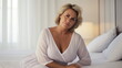 © Mickael - Very attractive mature women posing sitting at her bedroom looking at the camera.Attractive middle aged lady in nightdress lying on bed. Generative AI