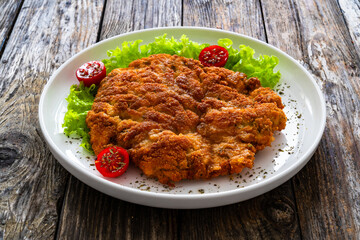 Wall Mural - Crispy breaded seared chicken cutlet with lemon slices and fresh vegetables on wooden table
