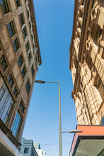 Looking Up At A Light Pole Against Blue Sky Between Two Historic Building Facades