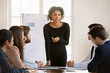 © fizkes - Young african American businesswoman stand lead meeting with multiracial colleagues in office, confident successful biracial female leader talk brainstorm with diverse employee at meeting or briefing