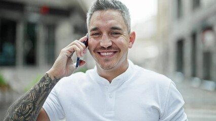 Wall Mural - Young hispanic man smiling confident talking on the smartphone at street