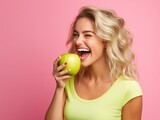 Beautiful happy woman in bright yellow top biting green crispy apple isolated on pink background, with copy space, concept of happiness, healthy food and losing weight.
