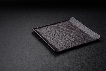 Empty black square ceramic plate on dark concrete background