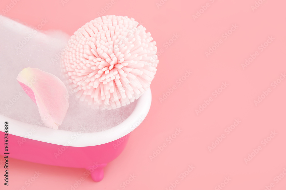 Small bathtub with foam and sponge on pink background