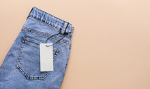 Blue Jeans With A Paper Label On A Beige Background. Black Friday Clothing Sale. Mock Up. Copy Space.