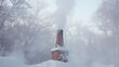 A brick chimney surrounded by newly fallen snow smoke slowly drifting from its top