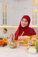 Wall Mural - Muslim woman making delicious salad with vegetables at white table in kitchen