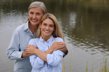 Wall Mural - Happy mature mother and her daughter hugging near pond, space for text