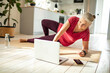 © Marko Geber - Senior caucasian woman doing yoga at home and using a laptop
