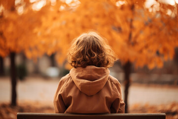 Wall Mural - Back view of a young girl kid sitting on a bench in an autumn park