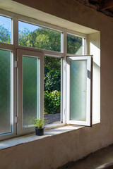 Wall Mural - Green plant in a pot on a windowsill with an open window in an old country house