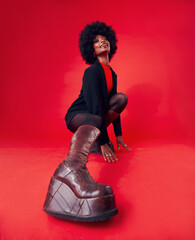 Fashion, boots and portrait of a black woman on a red background in studio to model trendy footwear. Style, clothes and smile with a happy young afro female posing for advertising or marketing