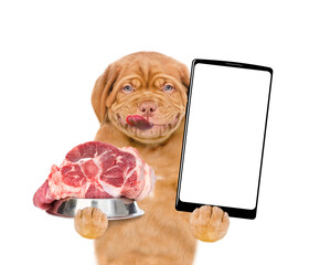 Poster - Happy licking lips puppy holding bowl of raw meat and shows empty screen of smartphone. isolated on white background