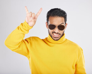 Poster - Man, sunglasses and horns sign in studio portrait, rock icon or hand gesture with clothes by white background. Young guy, model and devil fingers for attitude, fashion or crazy with emoji for culture