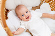 happy joyful baby in a wicker crib smiles or laughs, baby wakes up in the morning or falls asleep, newborn baby smiles, top view