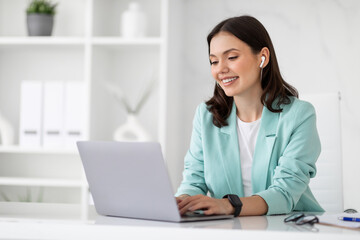 Wall Mural - Happy millennial european business lady in wireless headphones use computer to chat