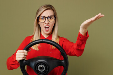 Young indignant furious angry woman she wears red shirt casual clothes glasses hold steering wheel driving car spread hand isolated on plain pastel green background studio portrait. Lifestyle concept.