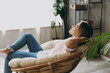 © ViDi Studio - Side profile back view calm blonde young woman wearing casual clothes sit in armchair look camera stay at home hotel flat rest relax spend free spare time in living room indoor. People lounge concept.