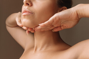 cropped shot of young caucasian woman touching under the chin with hands massaging her face on dark 