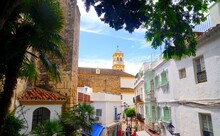 View Along An Alley In The Old Town Of Marbella With The Steeple Of The Catholic Church Iglesia De Nuestra Señora De La Encarnación Behind,, Costa Del Sol, Málaga, Andalusia, Spain