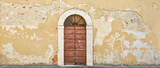Fototapeta Desenie - Rustic crumbling house wall with beautiful old door in Tuscany.
