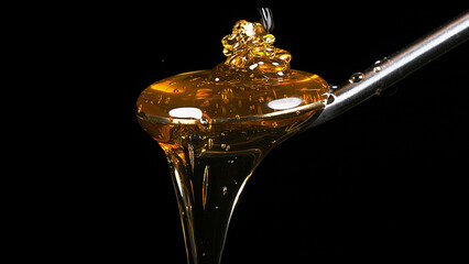 Wall Mural - Honey Flowing from Spoon against Black Background