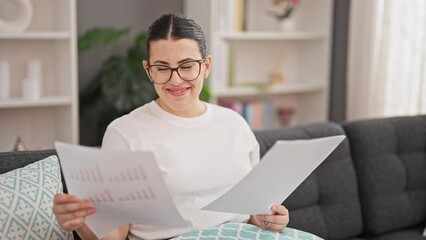 Canvas Print - Young beautiful hispanic woman reading documents sitting on sofa at home