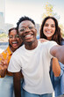 © Jose Calsina - Vertical portrait of a group of multiracial young student people smiling taking a selfie together. Happy african american teenager laughing with his cheerful friends. Classmates on friendly meeting