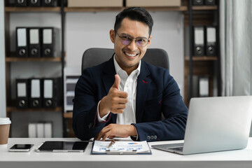 Happy Asian male businessman giving a thumbs up gesture of approval and success.