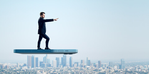 Aufkleber - User experiences for mobile concepts. Young man pointing forward on huge flying smartphone on wide bright blue sky background with mock up place.