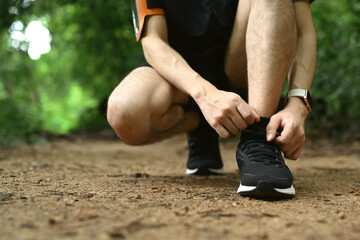 Unrecognizable male runner tying shoes laces, getting ready for trail run in forest. Sports, adventure and healthy lifestyle