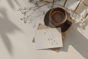 Winter still life. Blank Christmas greeting card, invitation mockup with dry flower in sunlight, shadows. Cup of coffee and white checkered plaid on table. Flatlay, top view. Copy space, no people