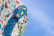 The climber climbs the artificial stone wall with the help of safety belts. An active young woman on a stone wall in a sports center. A girl trains on a rock climber in the open air. A beautiful, athl
