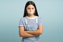 Sad Frustrated Teen Girl With Closed Tape Mouth On Turquoise Background Looks Down Stands In Closed Pose. Silence, Concealment Of Facts, Domestic Violence, Diet, Eating Disorders, Weak Women Rights.