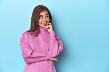 Wall Mural - Teen girl in cozy pink sweatshirt on blue relaxed thinking about something looking at a copy space.